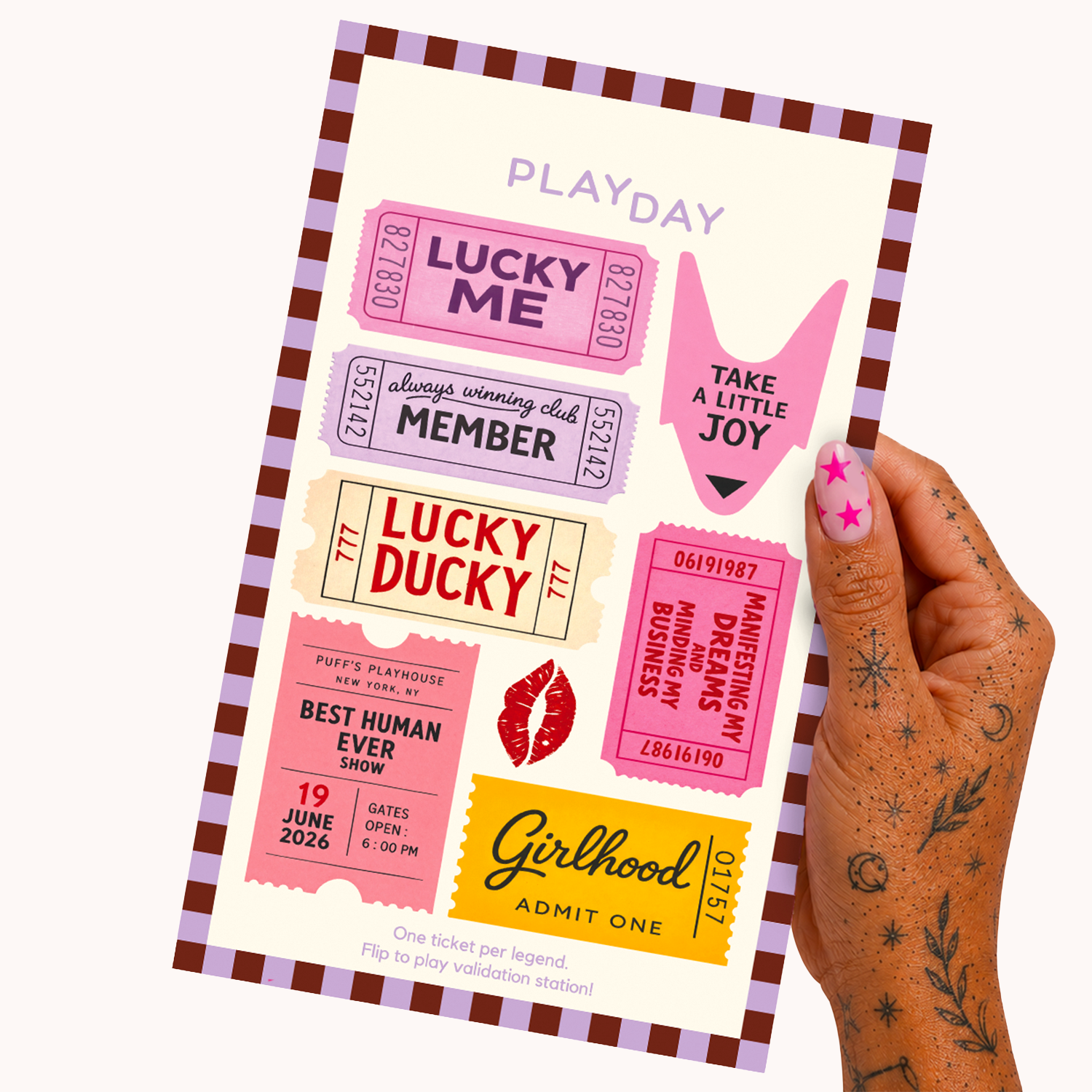 A hand with decorated nails holds a flip-top ticket sticker set labeled 'PLAYDAY'. The sheet contains multiple colorful ticket-shaped stickers with phrases like 'LUCKY ME', 'Lucky Ducky', 'Girlhood Admit One', and 'TAKE A LITTLE JOY' on a cream background with a purple border.