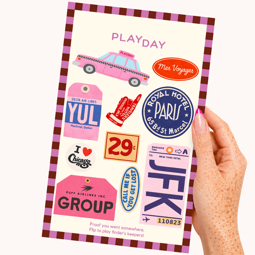 A hand with pink nail polish holds a PLAYDAY sticker sheet featuring colorful travel-themed stickers and text, set against a plain off-white background.